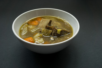 Delicious soup in white bowl over black background.