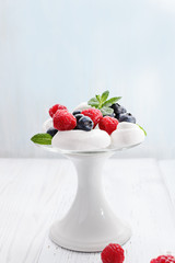 Pavlova - mini meringue cake with  fresh berries  on  white cake stand on old vintage wooden  background, copy space, close up, selective focus.