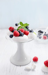 Pavlova - mini meringue cake with  fresh berries  on  white cake stand on old vintage wooden  background, copy space, close up, selective focus.