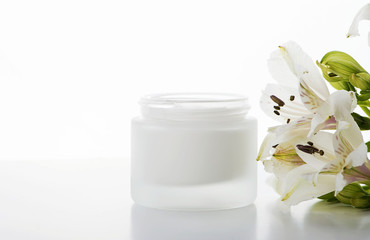 Close-up of bottle of skin cream.Next to lily flowers on white background. Isolated.