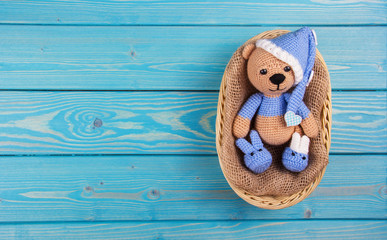 Obraz premium Small knitted bear lying in a basket on a blue wooden background. Teddy bears crocheted. Copy space