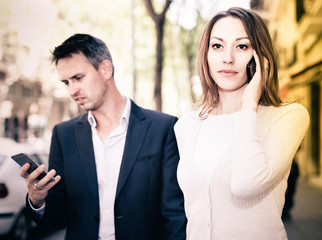 Couple strolling together and ignoring each other speaking on phones