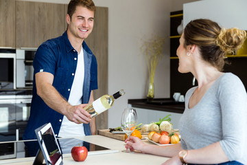 Handsome young man opening wine bottle while his wife using digital tablet in the kitchen.