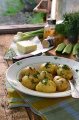 Organically grown new potatoes with butter and dill on wooden background. First spring harvest.