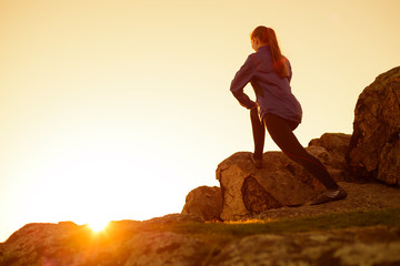 Young Fitness Woman Stretching her Legs in the Mountains at Sunset. Female Runner Doing Stretches Outdoor. Healthy Lifestyle Concept.