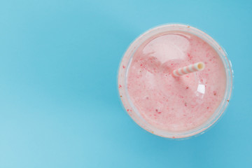 Top view of a strawberry smoothie in a plastic cup with a straw on a blue background. Pastel color. Summer & healthy lifestyle concept.