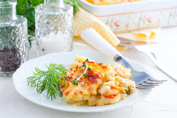 Portion of potato casserole with vegetables on a white plate, selective focus