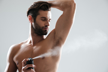 Horizntal image of young man using deodorant - obrazy, fototapety, plakaty