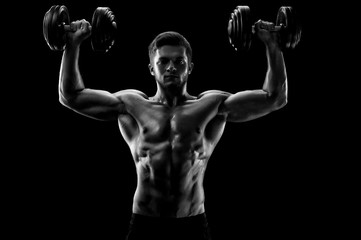 Black and white studio shot of a handsome young shirtless weightlifter exercising with dumbbells...