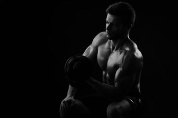 Monochrome low key light shot of a shirtless athletic man working out with dumbbells copyspace...