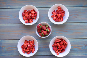 Heap of fresh strawberries in ceramic bowl on rustic blue wooden background.