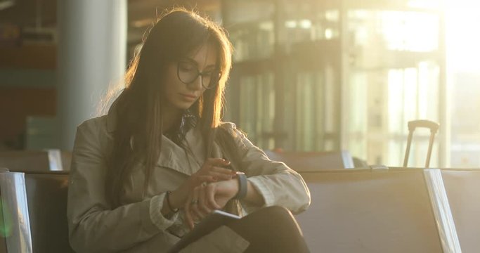Pretty young female passenger browsing tablet with backpack and carry on luggage at international airport, Checking her smart watch