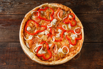 Delicious bright colorful pizza with tomato, paprika, chicken, ham, cheese and onion served on rustic wooden table, flat lay. Italian fast food.