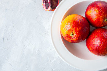 Fresh ripe whole and slices of blood oranges in a plate on a white stone background. Copy space and...