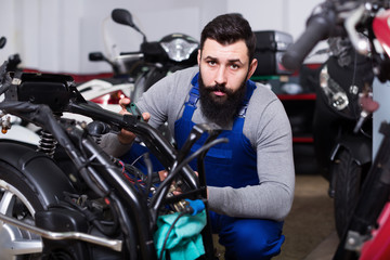 Fototapeta na wymiar Worker repairing failed scooter in motorcycle garage