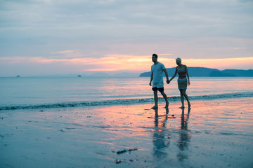 Fototapeta na wymiar Couple Walking Holding Hands On Beach At Sunset, Young Tourist Man And Woman On Sea Holiday While Summer Vacation