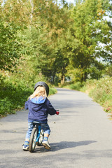 Fototapeta premium Child riding balance bike. Kid on bicycle in sunny park. Little girl ride glider bike on warm summer day. Preschooler learning to balance on run bicycle. Sport for kids