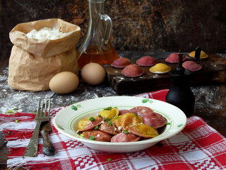 Fresh pink yellow beet dumplings or ravioli stuffed with ricotta cheese with butter sauce on wooden board on dark background. Space for text