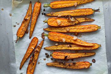 Roasted spring carrots on parchment with garlic, pepper peas and coriander on baking sheet. Selective focus