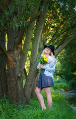 Young woman in a hat and with a bouquet of roses in the park.