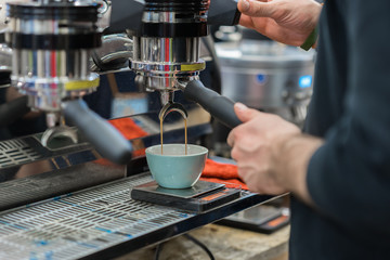 Close-up view hands of professional barista working in coffee house preparing espresso, waiting for coffee machine to finish pouring fresh drink into porcelain cup