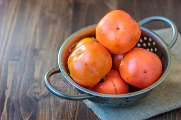 Persimmons in metal collander on wooden table.