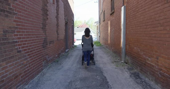 young mom slowly walks down birck alley way with stroller - away from camera