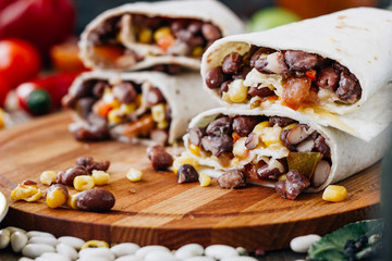 Nice vegetarian burrito over black table on wooden board.