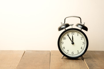 black vintage alarm clock close to the window present five minutes to twelve o'clock, midday or midnight