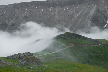 green mountains against the grey cliffs with fog and clouds