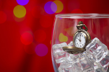 Vintage pocket watch on ice in wine glass on light bokeh background