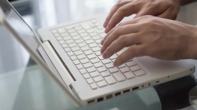 Close-up of a man typing on a laptop keyboard
