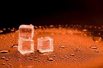 Water drop with ice cubes on lighting red background.