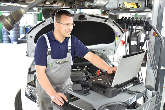 moderne Fehlersuche mit Diagnosecomputer in einer Autowerkstatt - KFZ Mechaniker repariert Fahrzeug