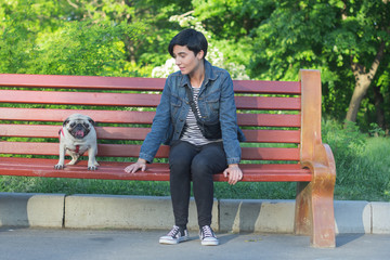 Portrait picture of young pretty woman in the park sit on bench, walk of female and pug in the summer park. 