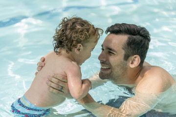 Hispanic Father and son playing in a pool.