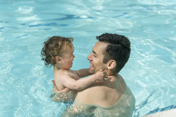 Hispanic Father and son playing in a pool.