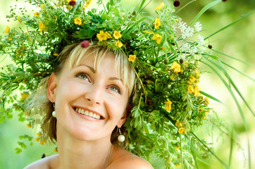Young happy girl in wreath of grasses and flowers. Summer day in a meadow.