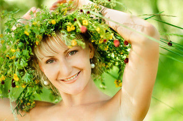Young happy girl in wreath of grasses and flowers. Summer day in a meadow.
