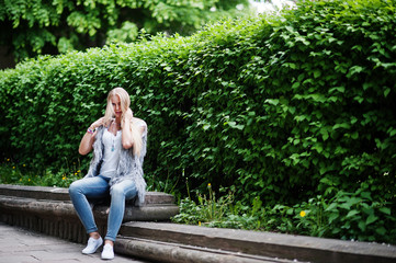 Stylish blonde woman wear at jeans and girl sleeveless with white shirt against bushes at street. Fashion urban model portrait.