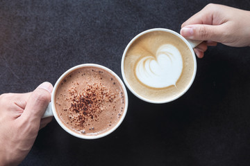 Top view image of man and woman's hands holding coffee and hot chocolate cups with wooden table background