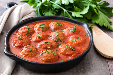 Meatballs with tomato sauce in iron frying pan on wooden table