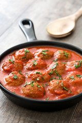 Meatballs with tomato sauce in iron frying pan on wooden table