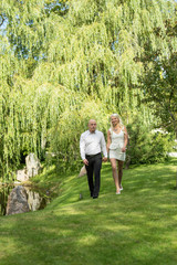 Happy couple holding hands and walking in grass. Man and woman in love. Young people resting in park, nature background