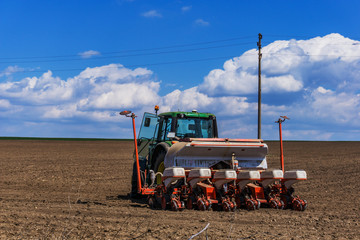 A beautiful landscape close up of a tractor with a seeder during planting the field. Fluffy clouds in the sky, a slight defocus with front bokeh. Concept agro culture.