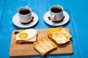 Two cups with coffee, toast and egg on a blue wooden table