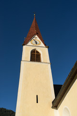 Fototapeta premium Chapel on the meadow. Bell tower, trees, shrubs and hilly green grassland. Heiliger Antoniuse church and houses in the evening light. Pitburger See, Taxegg, Salzburg, Austria, Europe