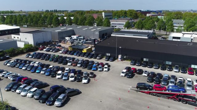Aerial over small temporary car lot to store new cars for resale and car dealers who do not have free space for storage on right side still a truck carrying cars is parked on lot with new shipment 4k