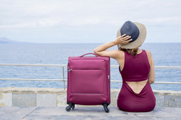Fototapeta premium The young woman seated with her suitcase, thinks about her next travel. 