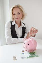 Obraz na płótnie Canvas Woman dropping money into piggy bank